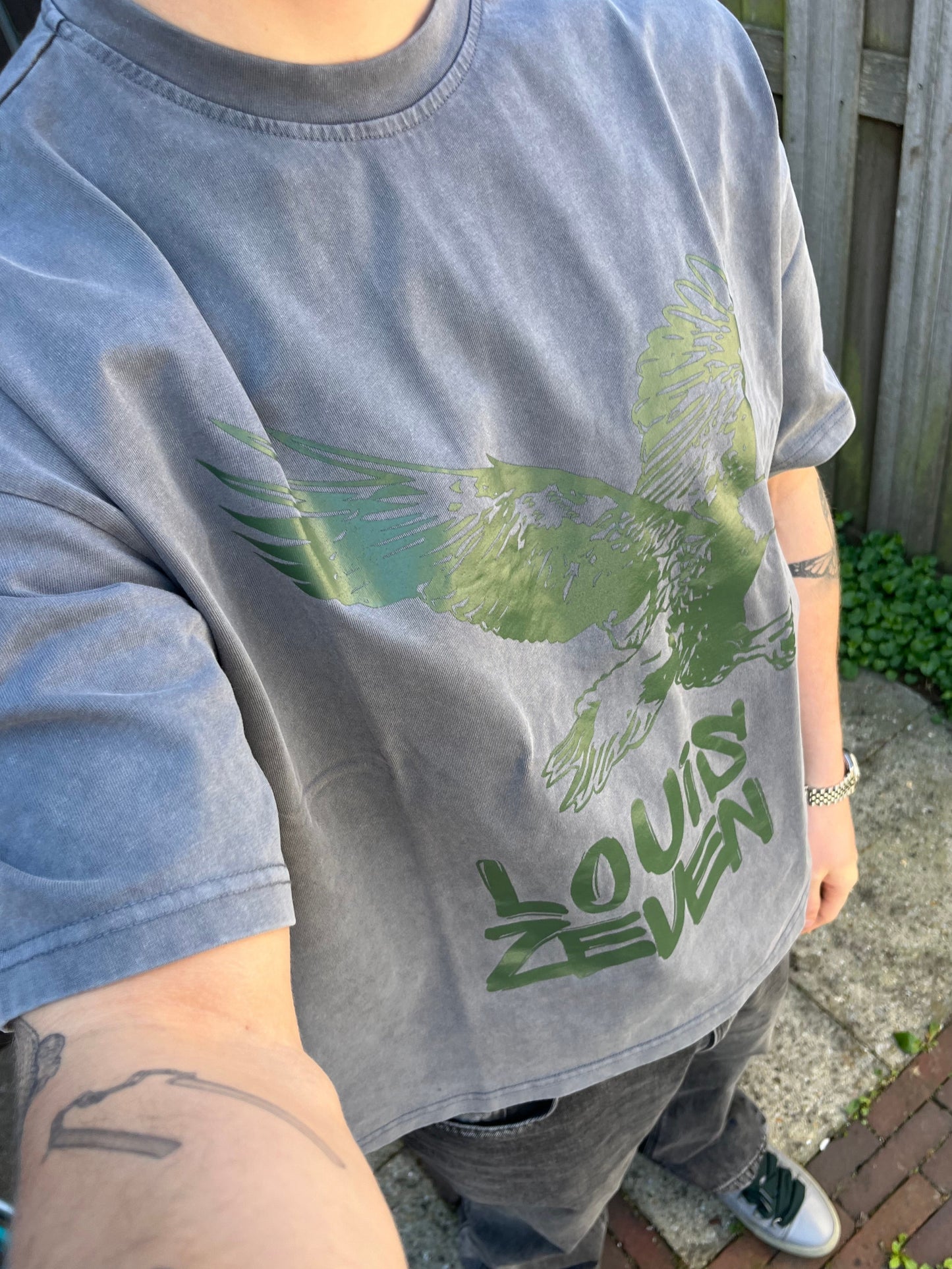 Man draagt grijs Louis Zeven boxy shirt met adelaar-print, streetwear stijl voor heren