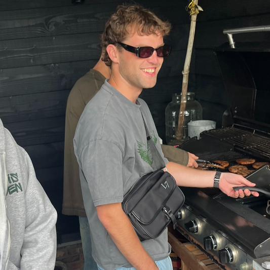 Man draagt grijs Louis Zeven boxy shirt met adelaar-print. Ook draagt hij een nylon messenger bag